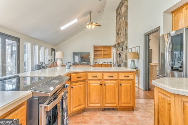 kitchen featuring light tile patterned flooring, a skylight, high vaulted ceiling, appliances with stainless steel finishes, and ceiling fan