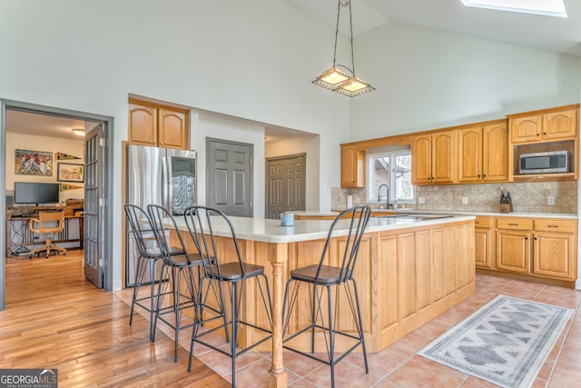 kitchen featuring a kitchen island, appliances with stainless steel finishes, high vaulted ceiling, a skylight, and decorative backsplash