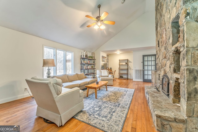 living room with ceiling fan, high vaulted ceiling, a stone fireplace, and light hardwood / wood-style floors