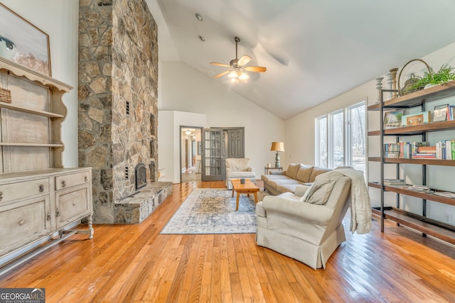 living room featuring ceiling fan, high vaulted ceiling, a fireplace, and light hardwood / wood-style floors