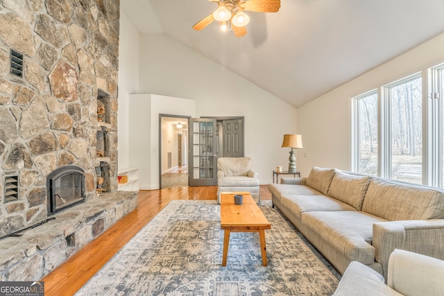 living room with lofted ceiling, ceiling fan, a stone fireplace, french doors, and light wood-type flooring