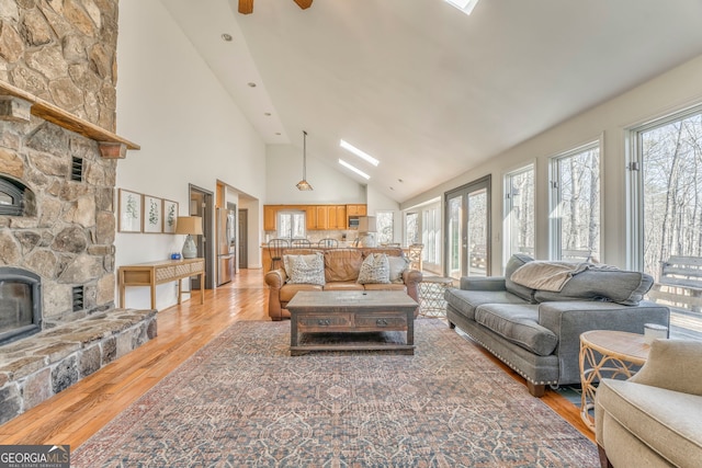 living room with a stone fireplace, high vaulted ceiling, and light hardwood / wood-style floors