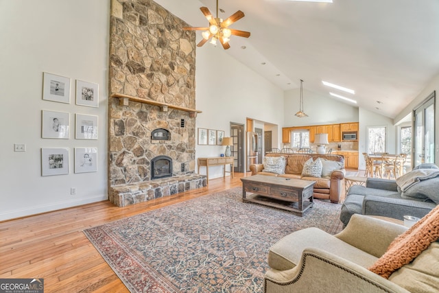 living room featuring a stone fireplace, high vaulted ceiling, ceiling fan, and light wood-type flooring