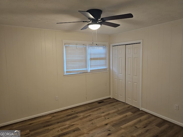 unfurnished bedroom featuring dark wood-type flooring, a textured ceiling, ornamental molding, a closet, and ceiling fan