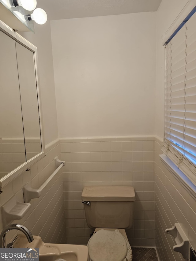 bathroom with toilet, sink, and tile walls