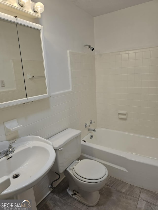 full bathroom featuring tiled shower / bath, sink, tile walls, and toilet