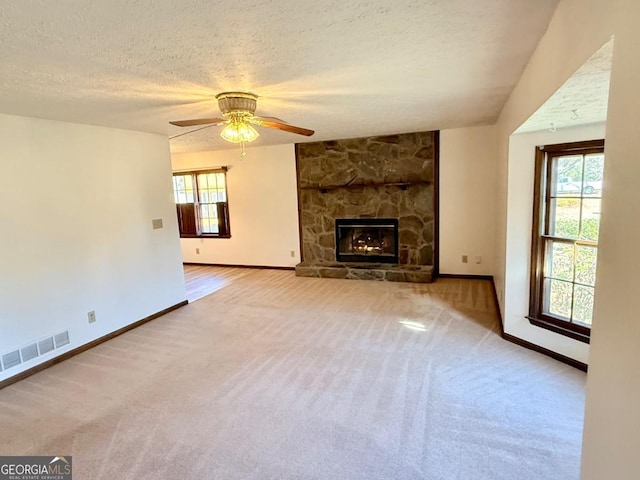 unfurnished living room featuring a stone fireplace, carpet floors, a textured ceiling, and ceiling fan