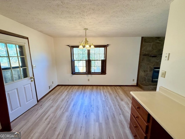 unfurnished dining area featuring a healthy amount of sunlight, an inviting chandelier, a textured ceiling, and light hardwood / wood-style flooring