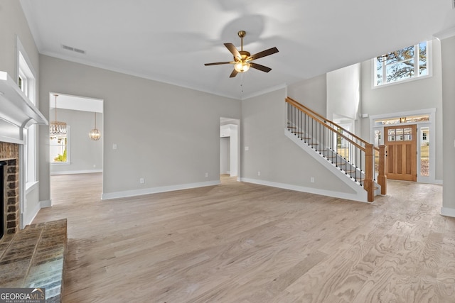 unfurnished living room featuring ceiling fan with notable chandelier, ornamental molding, a fireplace, and light hardwood / wood-style floors