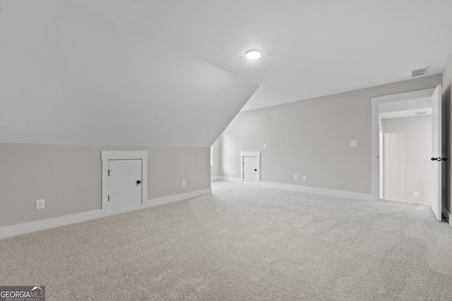 additional living space featuring vaulted ceiling and light colored carpet