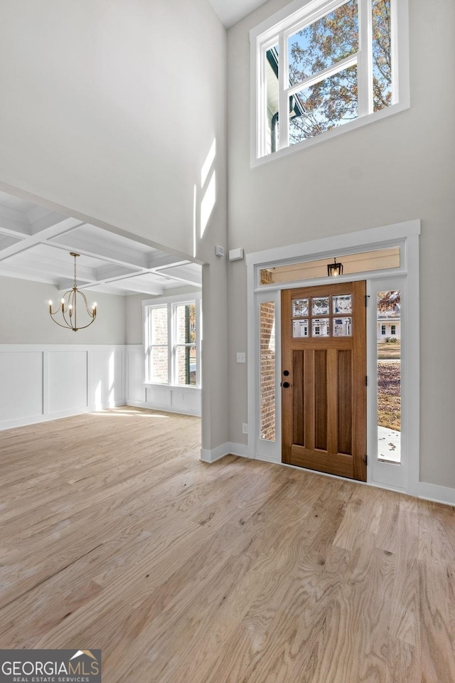 foyer entrance featuring coffered ceiling, light wood-type flooring, beam ceiling, and a notable chandelier