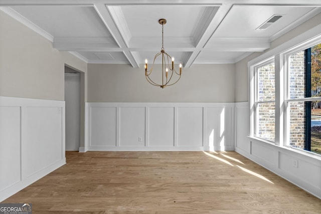 unfurnished dining area featuring beam ceiling, coffered ceiling, light hardwood / wood-style floors, crown molding, and an inviting chandelier