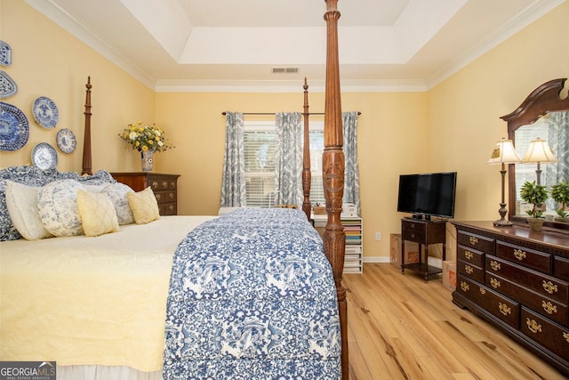 bedroom with crown molding, a tray ceiling, and light wood-type flooring