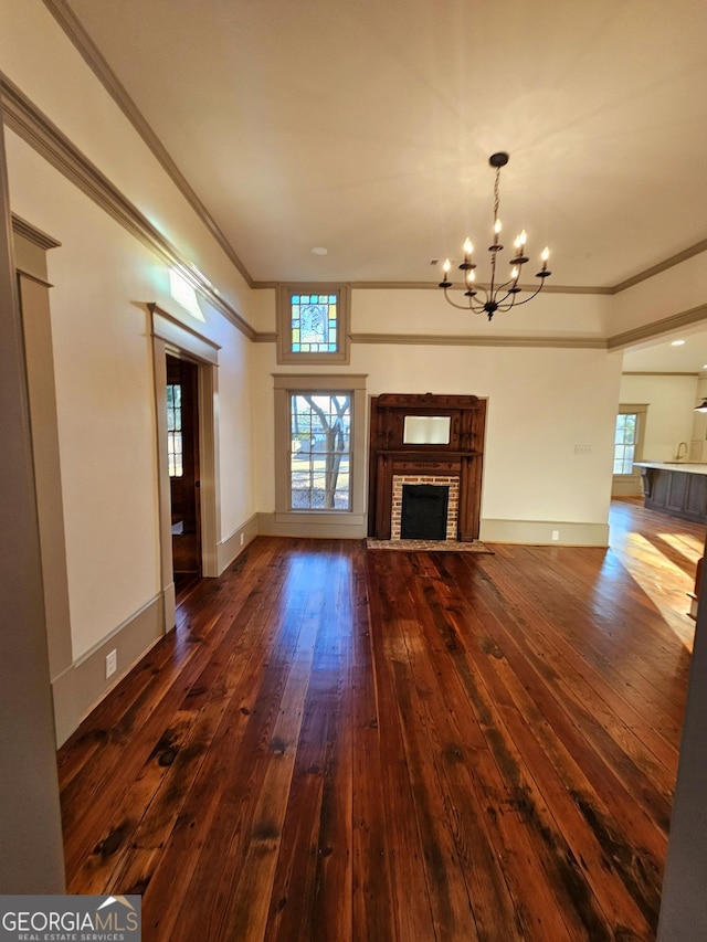 unfurnished living room with ornamental molding, a brick fireplace, dark wood-type flooring, and an inviting chandelier