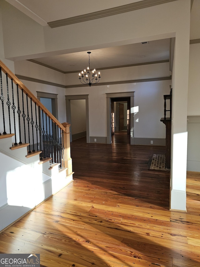 staircase featuring hardwood / wood-style flooring, ornamental molding, and a notable chandelier