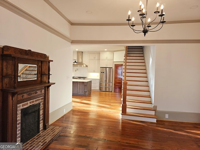 unfurnished living room with an inviting chandelier, ornamental molding, light hardwood / wood-style floors, and a brick fireplace