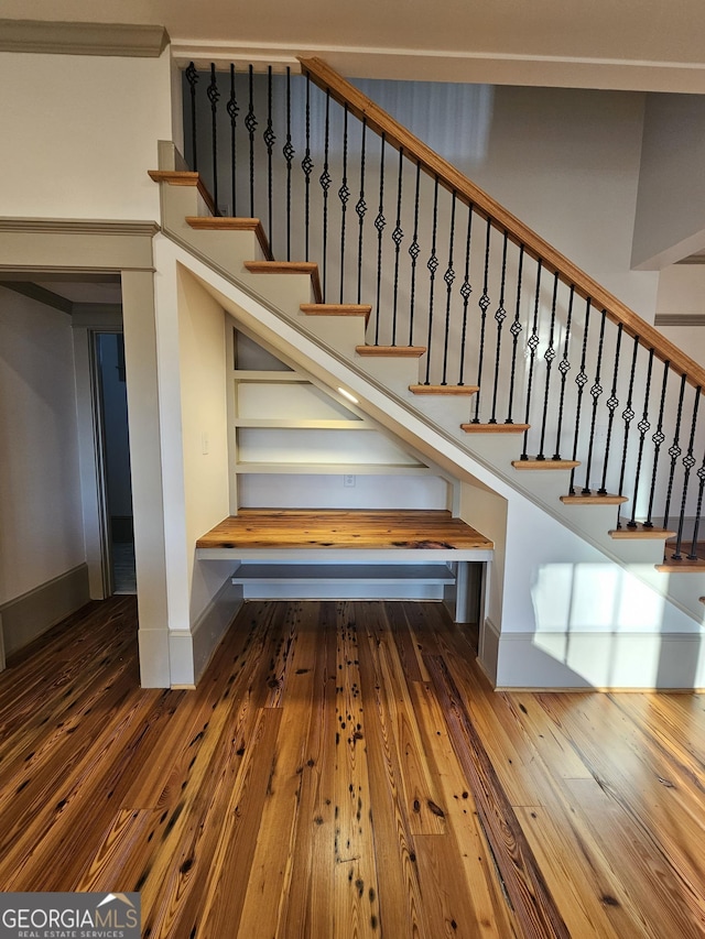 stairs with ornamental molding and hardwood / wood-style floors