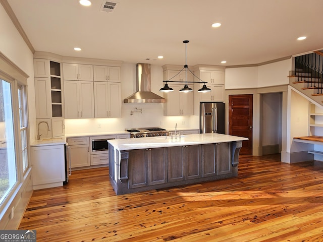 kitchen featuring built in microwave, high end refrigerator, wood-type flooring, a kitchen island with sink, and wall chimney range hood