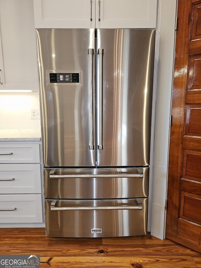 interior details featuring white cabinetry, high end refrigerator, light stone countertops, and light hardwood / wood-style floors