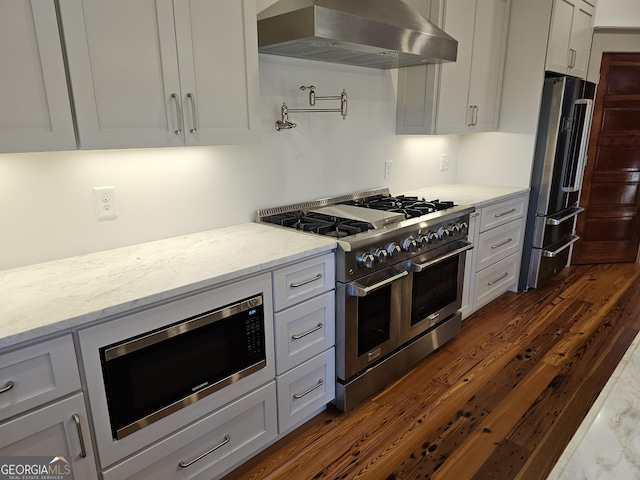 kitchen featuring high end appliances, light stone countertops, range hood, and dark hardwood / wood-style floors