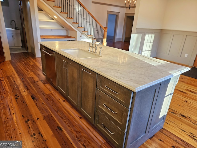 kitchen featuring dark hardwood / wood-style floors, sink, stainless steel dishwasher, light stone counters, and a center island with sink