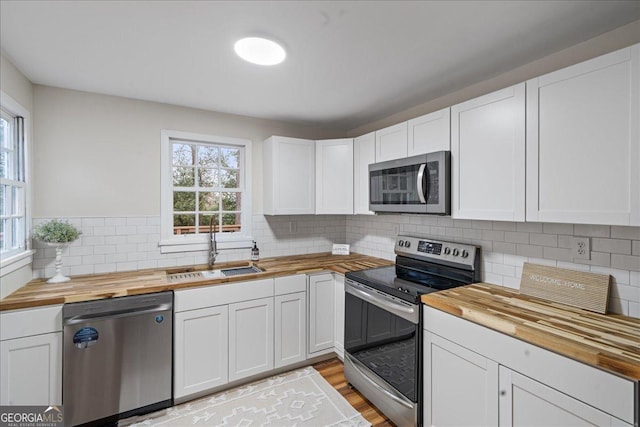 kitchen with butcher block counters, sink, stainless steel appliances, and white cabinets