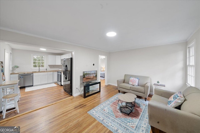 living room with ornamental molding, sink, and light hardwood / wood-style flooring