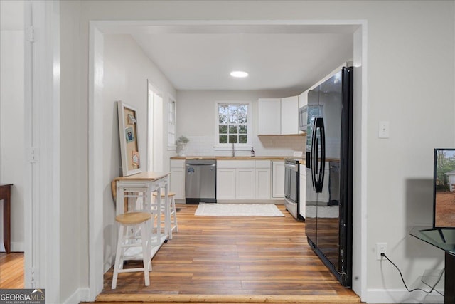 kitchen with white cabinetry, stainless steel appliances, light hardwood / wood-style floors, and backsplash