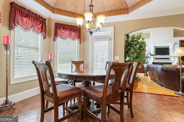 dining space with a notable chandelier, tile patterned floors, ornamental molding, and a raised ceiling