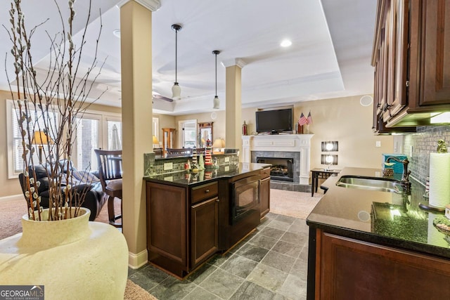 kitchen featuring pendant lighting, sink, a tiled fireplace, dark brown cabinetry, and a tray ceiling