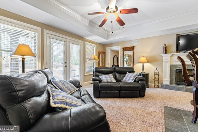 living room featuring ceiling fan, carpet, a tray ceiling, ornamental molding, and a tiled fireplace