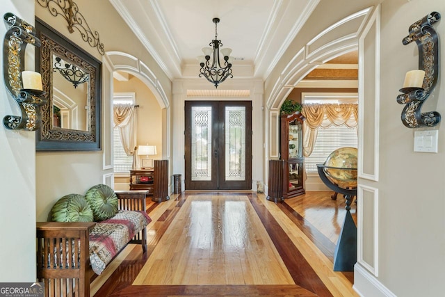 entryway with crown molding, hardwood / wood-style floors, an inviting chandelier, and french doors