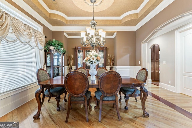 dining room with a notable chandelier, a tray ceiling, ornamental molding, and light wood-type flooring