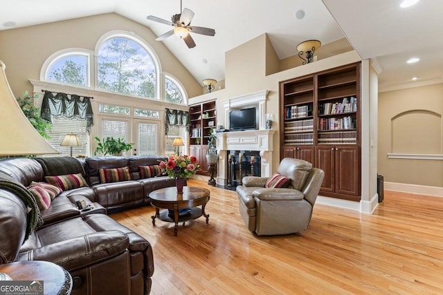 living room featuring built in shelves, high vaulted ceiling, light hardwood / wood-style flooring, ceiling fan, and a high end fireplace