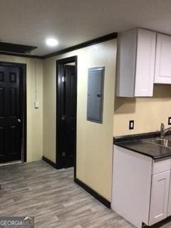 kitchen with sink, electric panel, white cabinets, and light wood-type flooring