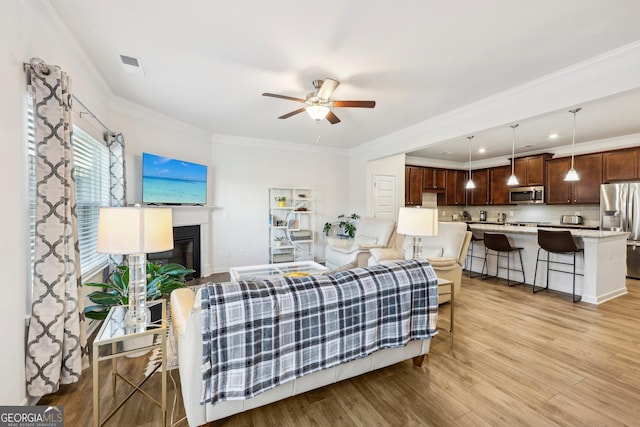 living room featuring ornamental molding, ceiling fan, and light wood-type flooring