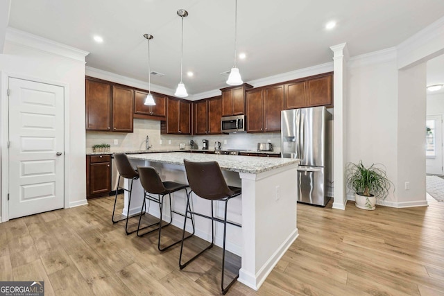 kitchen with light stone counters, appliances with stainless steel finishes, a kitchen island, pendant lighting, and decorative backsplash