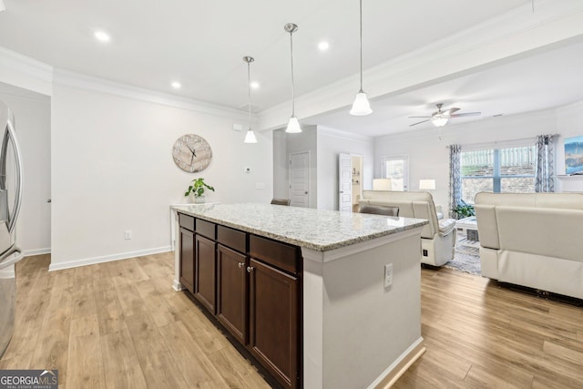 kitchen with hanging light fixtures, dark brown cabinets, light stone counters, light hardwood / wood-style floors, and a kitchen island