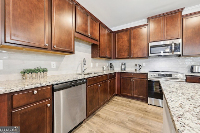 kitchen with appliances with stainless steel finishes, sink, backsplash, light stone counters, and light hardwood / wood-style flooring