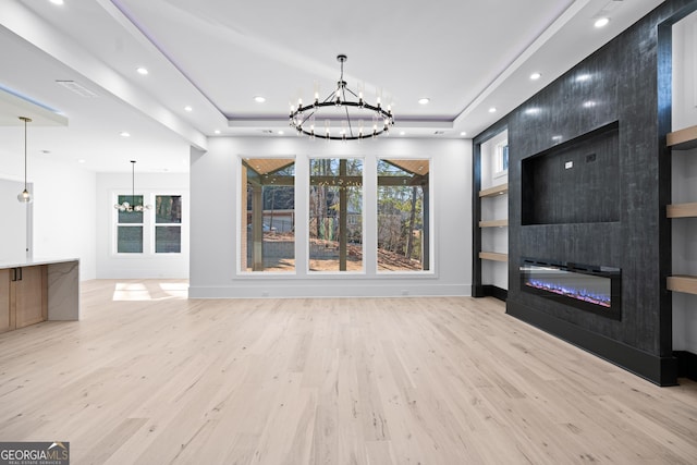 unfurnished living room with a notable chandelier, built in shelves, a fireplace, and light wood-type flooring