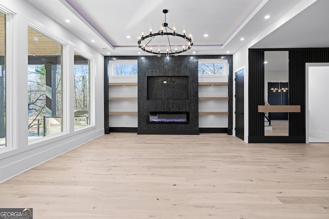 unfurnished living room featuring a raised ceiling, a fireplace, a chandelier, and light hardwood / wood-style flooring