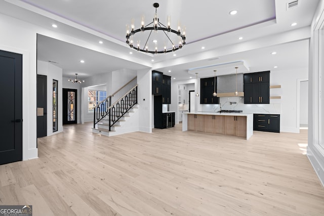 kitchen featuring light hardwood / wood-style flooring, a spacious island, a notable chandelier, decorative backsplash, and decorative light fixtures