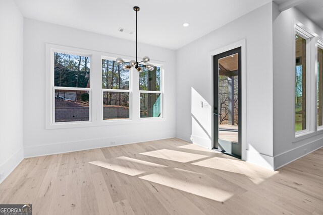 unfurnished dining area with plenty of natural light, light hardwood / wood-style floors, and a notable chandelier