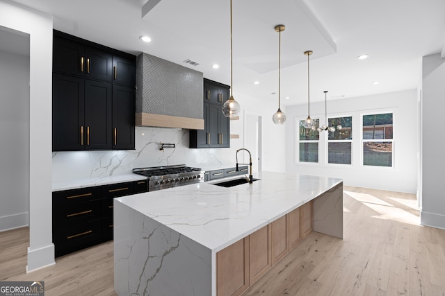 kitchen featuring hanging light fixtures, sink, an island with sink, and range