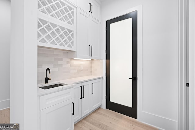 bar featuring tasteful backsplash, white cabinetry, sink, and light hardwood / wood-style flooring