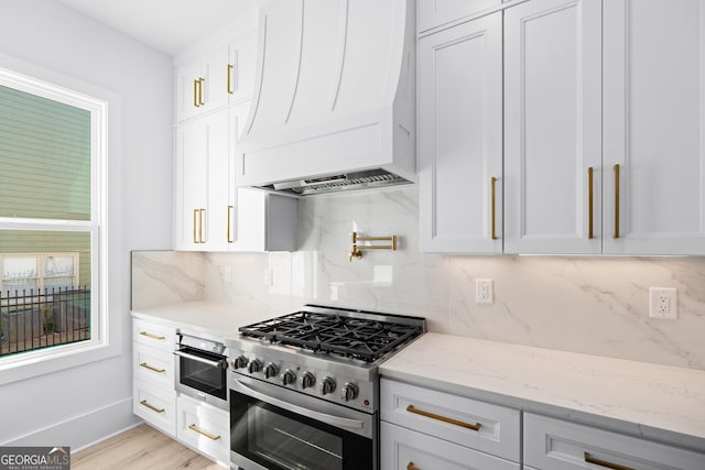 kitchen with stainless steel appliances, light stone countertops, custom range hood, and white cabinets