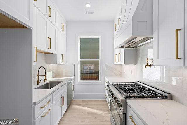 kitchen featuring premium range hood, sink, white cabinetry, stainless steel appliances, and light stone countertops