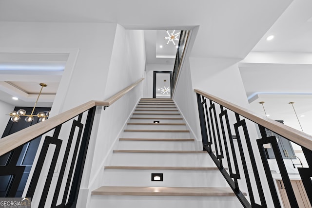 stairway with a raised ceiling and a chandelier