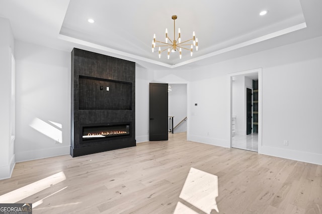 unfurnished living room featuring a notable chandelier, a tray ceiling, light hardwood / wood-style flooring, and a fireplace