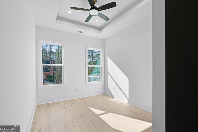 unfurnished room featuring ceiling fan, a tray ceiling, and light hardwood / wood-style flooring